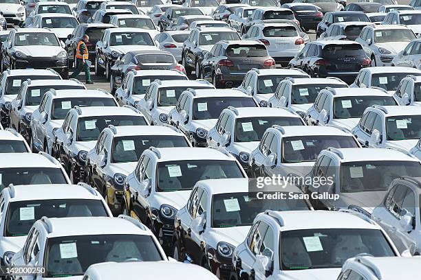 Worker walks past freshly-assembled Porsche Cayenne and Panamera cars standing on a parking lot before shipping at the Porsche factory on March 28,...