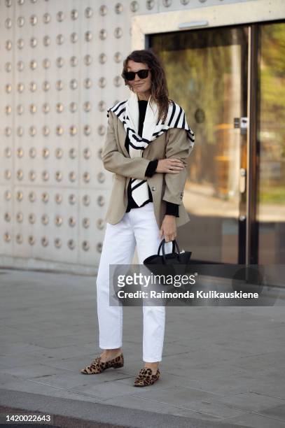 Caroline Winberg wearing white pants, black top, beige jacket, white and black striped sweater, black bag and animal print brown shoes outside...