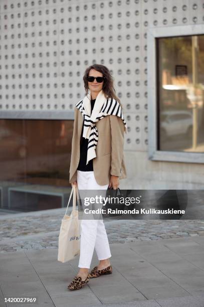 Caroline Winberg wearing white pants, black top, beige jacket, white and black striped sweater, black bag and animal print brown shoes outside...