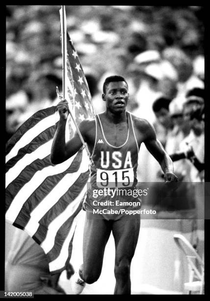 American athlete Carl Lewis celebrates with a stars and stripes national flag during competition at the 1984 Summer Olympics inside the Memorial...