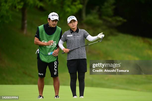 Sakura Yokomine of Japan lines up a putt with her caddie and husband Yotaro Morikawa on the 18th green during the first round of Golf5 Ladies at...