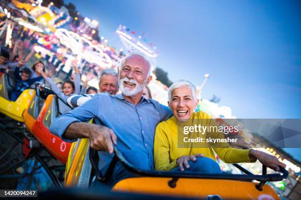 happy senior couple having fun while riding on rollercoaster at amusement park. - couple rollercoaster stock pictures, royalty-free photos & images