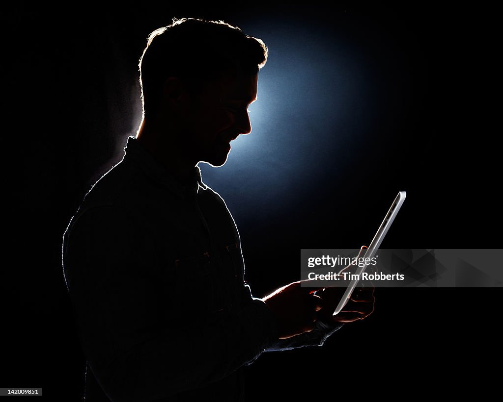 Young man using digital tablet in silhouette.