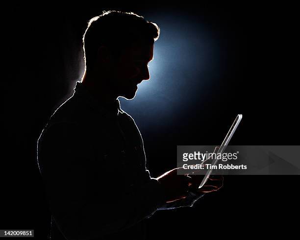 young man using digital tablet in silhouette. - spotlight person stock pictures, royalty-free photos & images