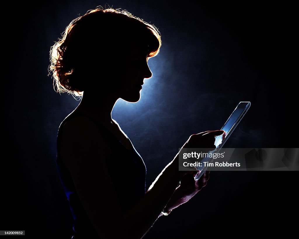 Young woman using digital tablet in silhouette.