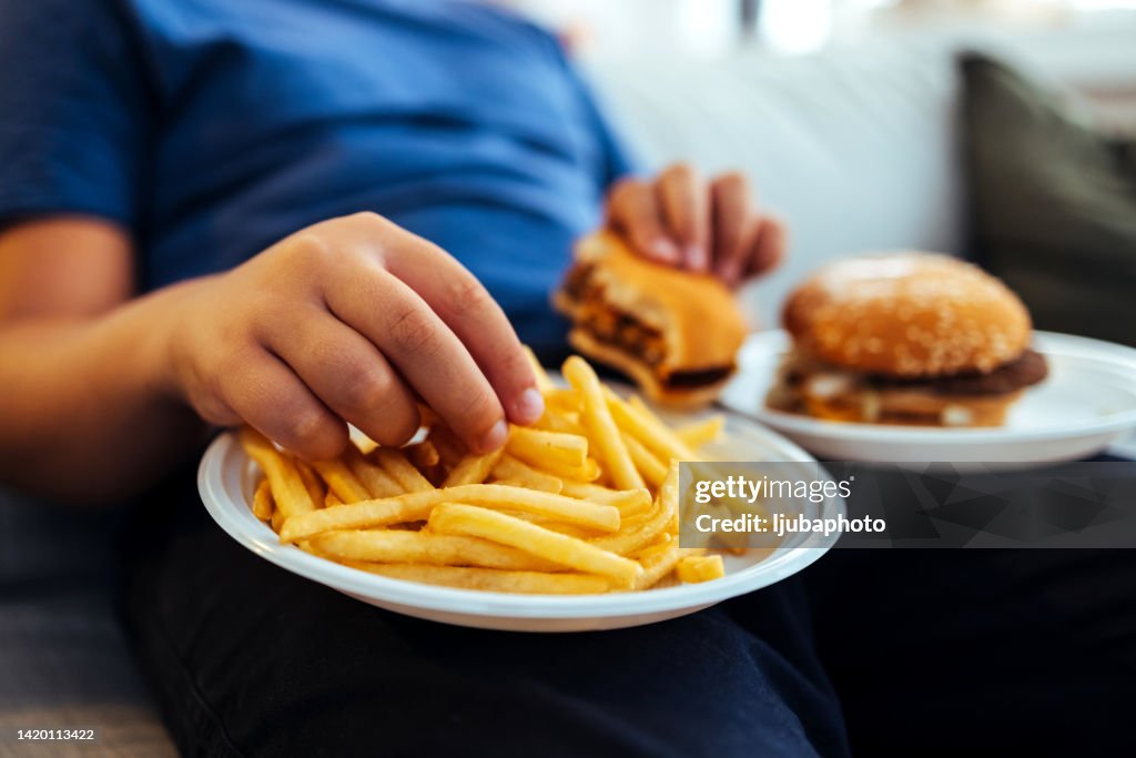 Adolescente con sobrepeso que come demasiada comida frita