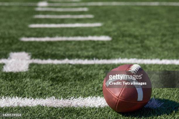 american football ball at yard line markers on playing field - footballs stockfoto's en -beelden