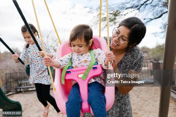 mother with daughters (2-3, 8-9) on playground swings - mother child swing stock pictures, royalty-free photos & images