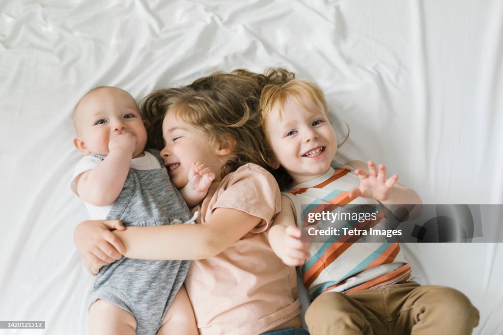 Siblings (6-11 months, 2-3) hugging on bed