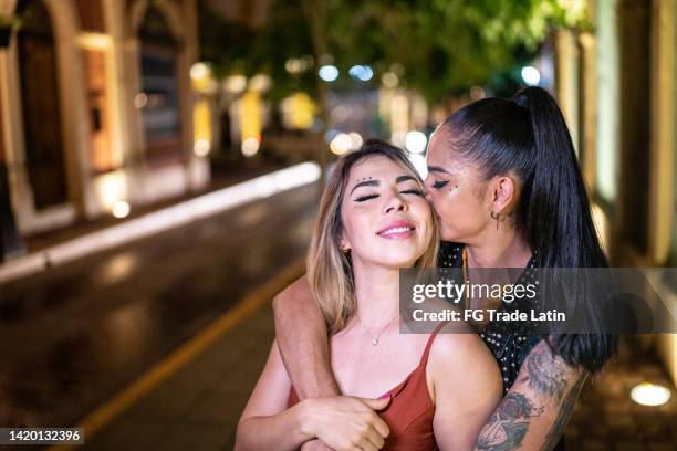 mid adult woman kissing her girlfriend while walking and having fun outdoors - lesbians kissing stock pictures, royalty-free photos & images