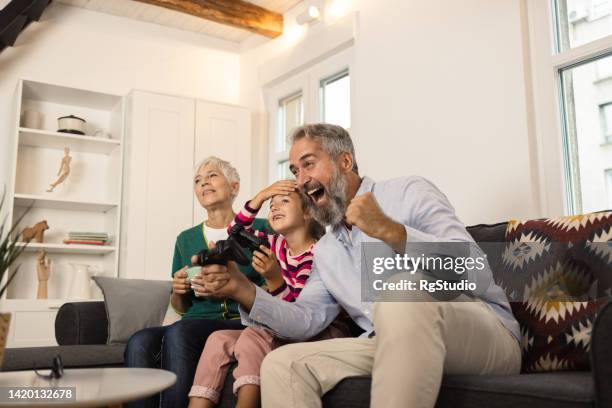 happy senior couple playing video games with their cute granddaughter - air conditioner family stock pictures, royalty-free photos & images