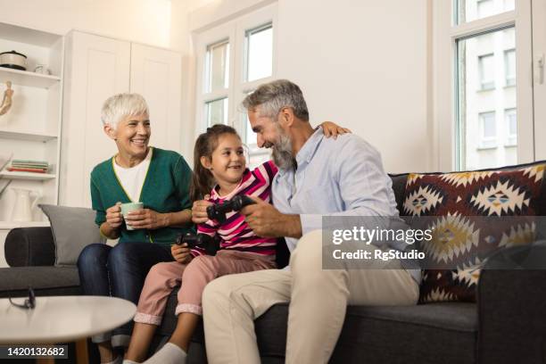 happy grandparents enjoying while playing video games with their cute granddaughter - air conditioner family stock pictures, royalty-free photos & images
