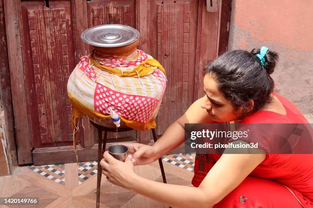 mujeres indias sedientas llenando un vaso de agua de una olla de barro en casa - ollas de barro fotografías e imágenes de stock