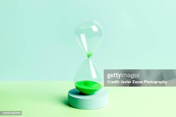 green colored sand hourglass on green background - clocks go forward foto e immagini stock