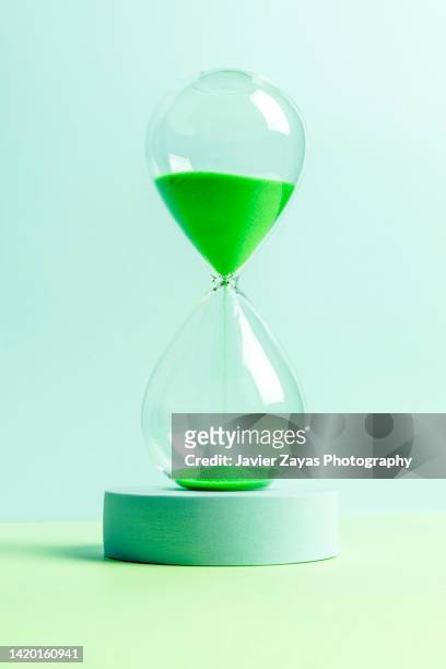 green colored sand hourglass on green background - early termination foto e immagini stock