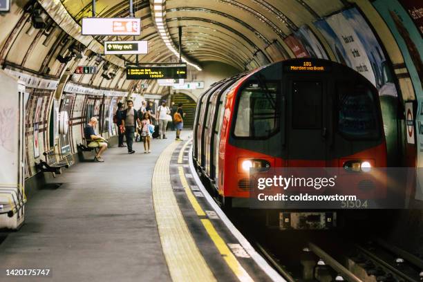 commuters on platform waiting to board subway train in london, uk - london underground stockfoto's en -beelden
