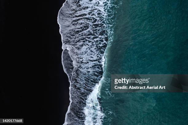 drone perspective showing waves washing onto a black sand beach, iceland - paysage volcanique photos et images de collection
