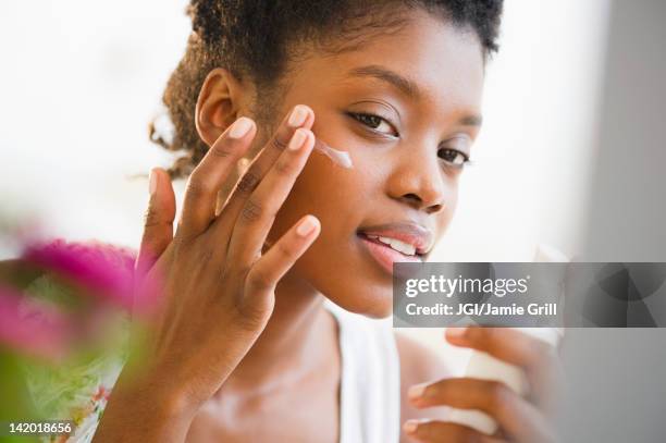 black woman putting on face lotion - lotion photos et images de collection