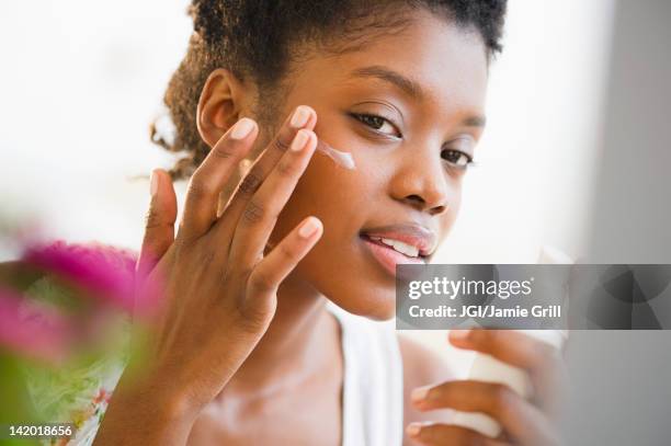 black woman putting on face lotion - skincare stockfoto's en -beelden