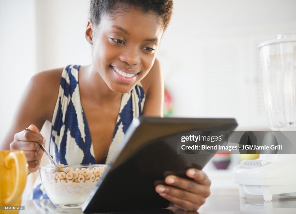 Black woman using digital tablet and eating cereal