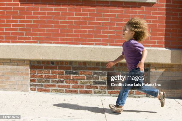 mixed race boy running on sidewalk - boy in wind stock-fotos und bilder