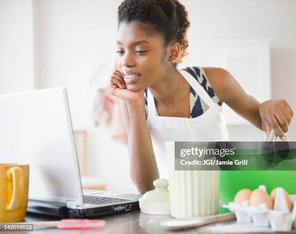 black woman cooking and looking at recipe on laptop - female whipping stock-fotos und bilder