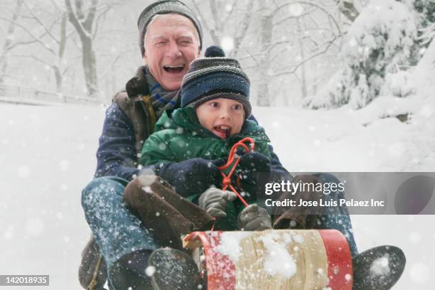 caucasian man sledding with grandson in the snow - grandfather child snow winter stock pictures, royalty-free photos & images