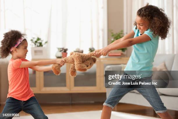 mixed race sisters fighting over teddy bear - pull foto e immagini stock