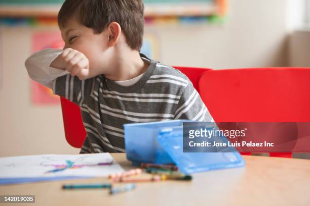caucasian boy blowing nose in classroom - blowing nose stock pictures, royalty-free photos & images