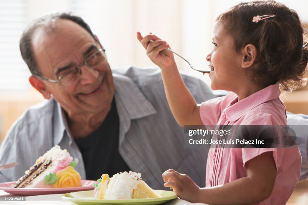 Hispanic girl and grandfather eating birthday cake