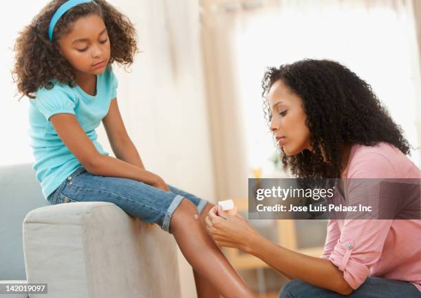 mixed race mother putting bandage on daughter - knees together fotografías e imágenes de stock