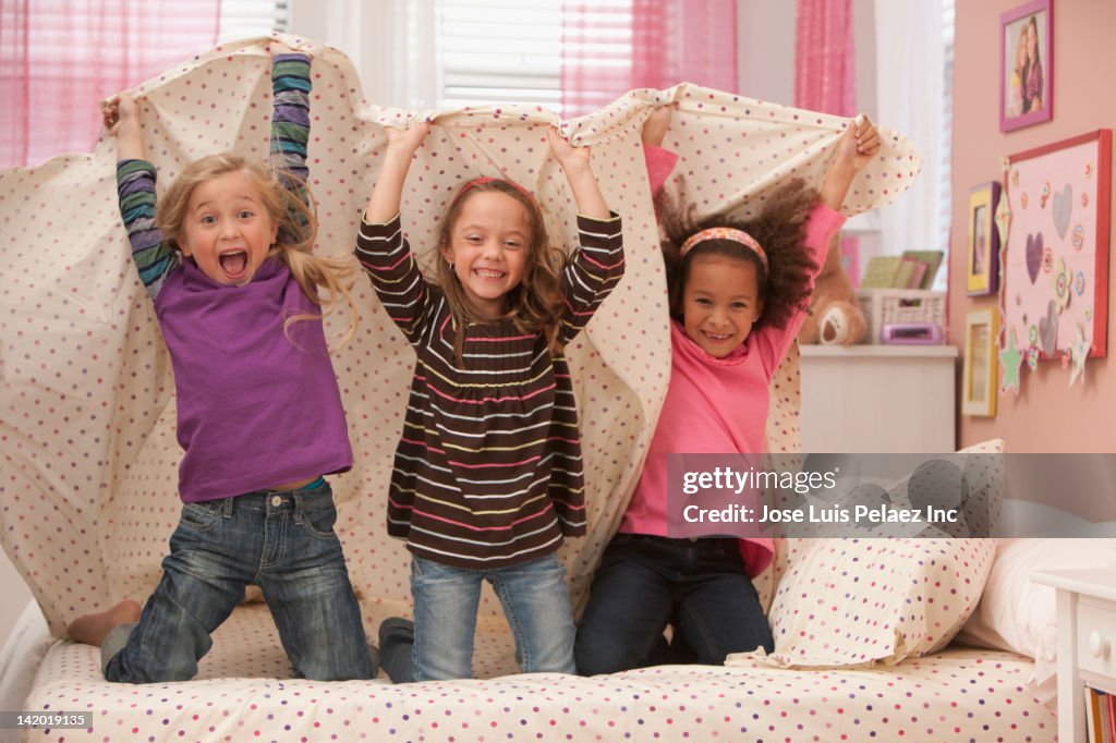 Laughing girls playing underneath bed sheet