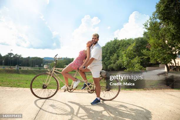 young couple riding tandem bicycle - tandem stock pictures, royalty-free photos & images