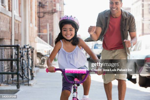 father teaching daughter to ride bicycle - encouragement stock pictures, royalty-free photos & images