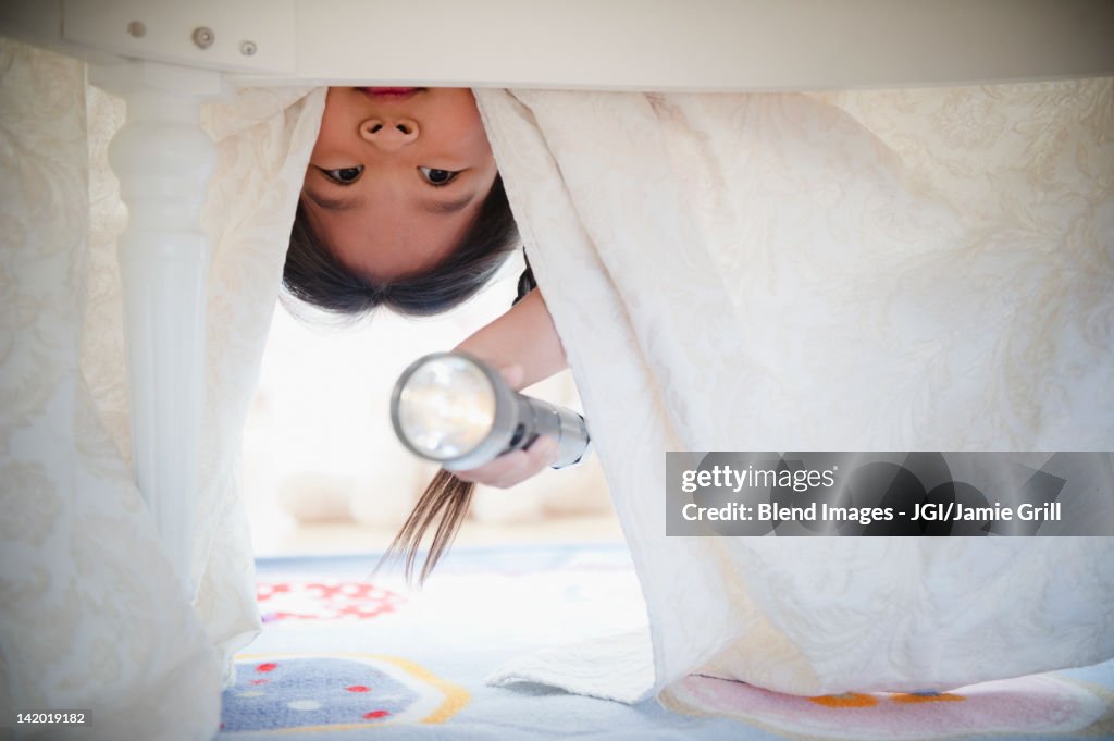 Korean girl looking under bed with flashlight