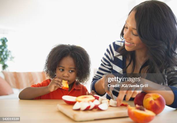 african american mother cutting fruit for son - mother and child snacking stockfoto's en -beelden