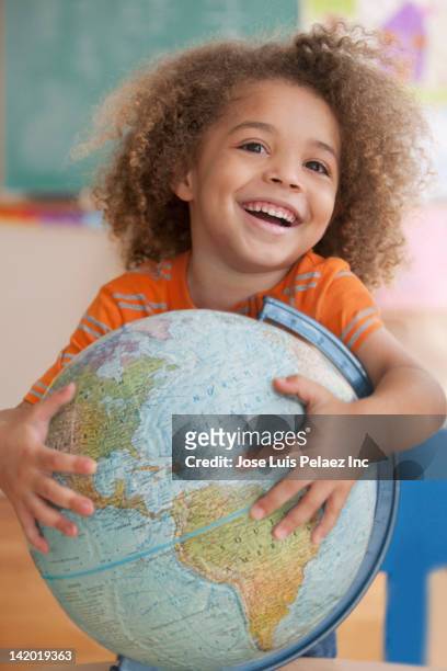 mixed race boy holding globe - international day of happiness stock-fotos und bilder