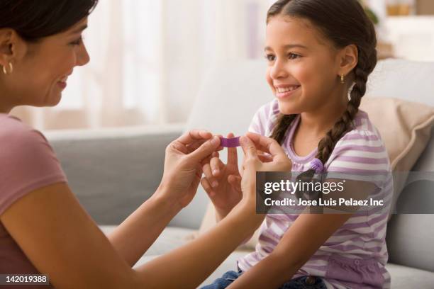 mother putting bandage on daughter's finger - pflaster stock-fotos und bilder