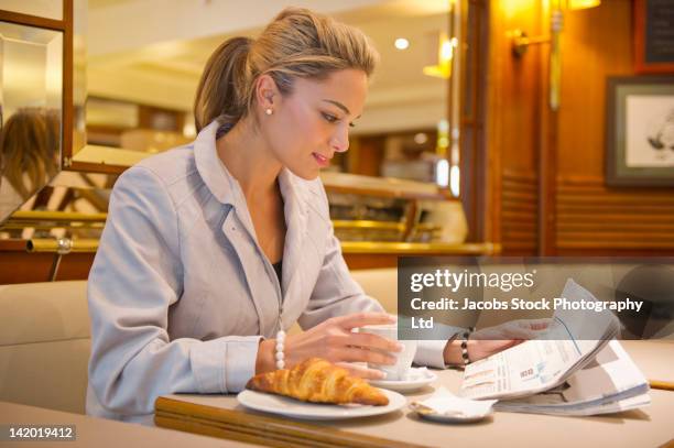 hispanic woman reading paperwork and having breakfast in cafe - the weekend in news around the world stockfoto's en -beelden