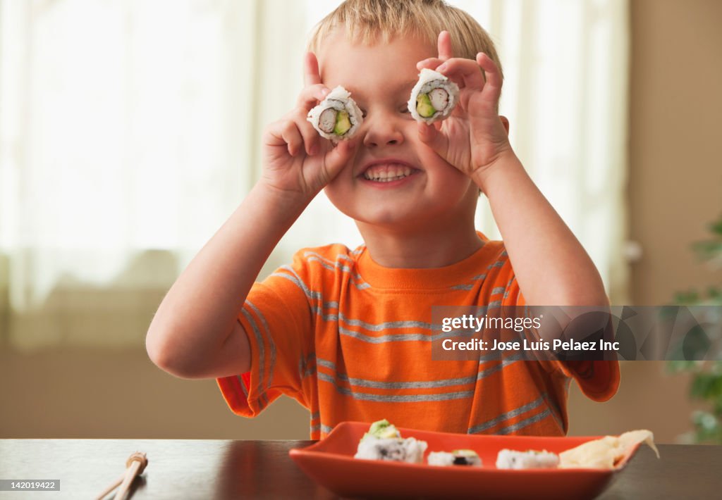 Caucasian boy holding sushi in front of his eyes