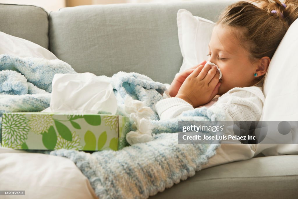 Caucasian girl laying on couch blowing her nose