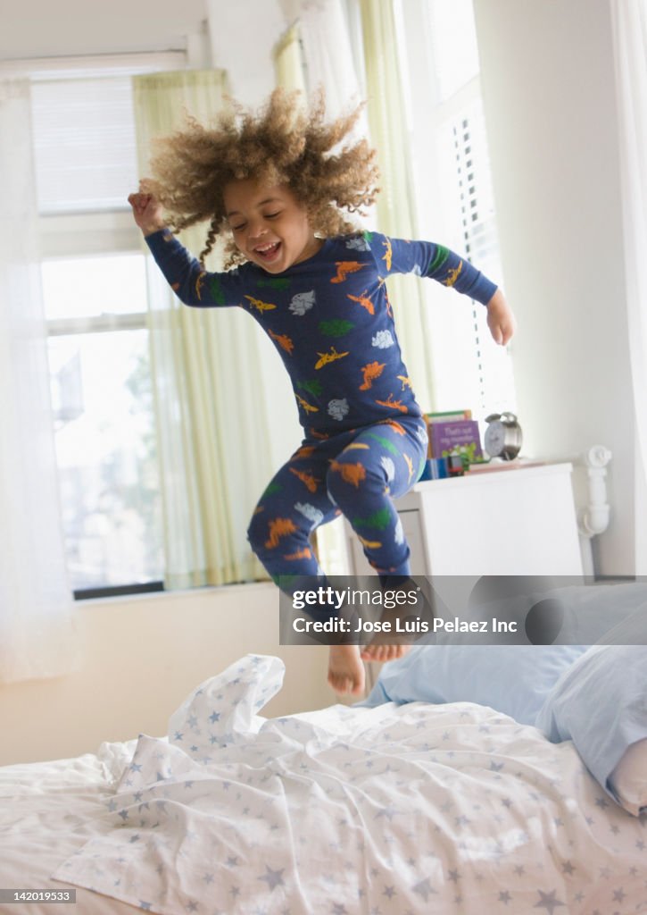 Mixed race boy jumping on bed