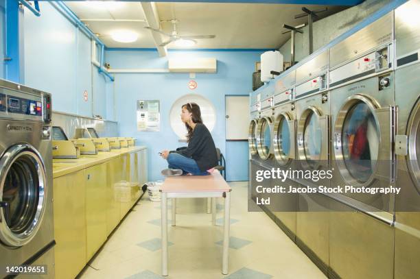 hispanic woman doing laundry in self-service laundry facility - wäscherei stock-fotos und bilder