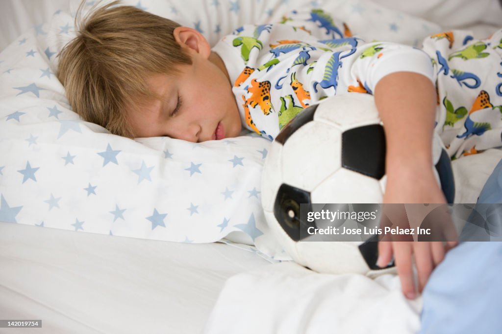 Caucasian boy sleeping in bed with soccer ball