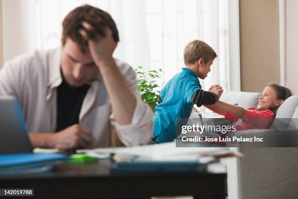 caucasian children playing on sofa while father works - annoying brother stock pictures, royalty-free photos & images