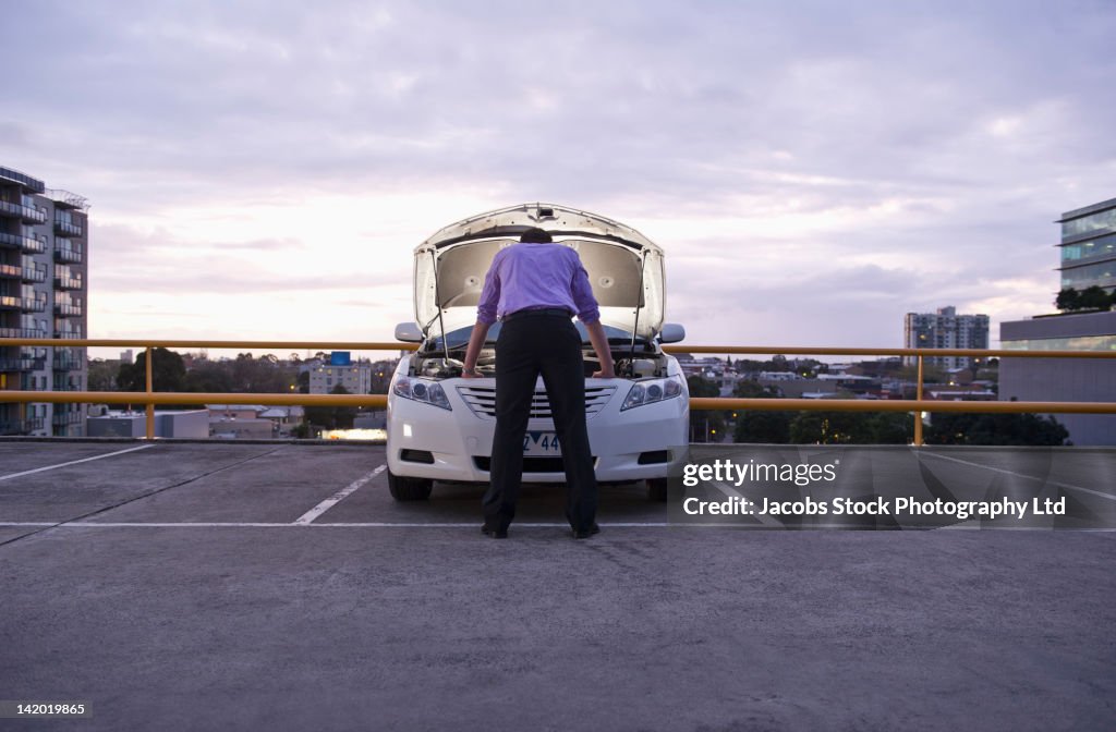 Caucasian businessman checking underneath automobile hood