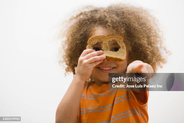 mixed race boy looking through holes in slice of bread - les-bras-écartés photos et images de collection