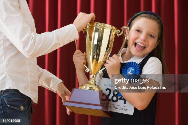 caucasian girl standing on stage wearing competition number and receiving trophy - receiving trophy stock pictures, royalty-free photos & images