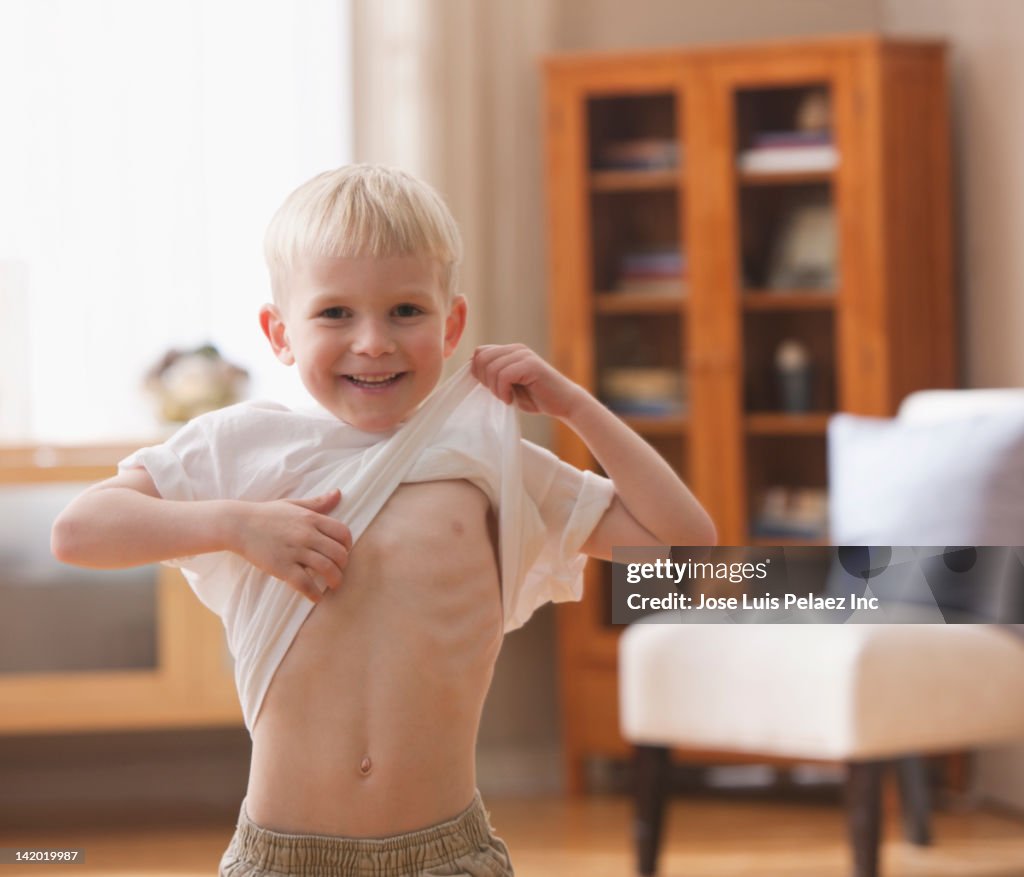 Caucasian boy lifting shirt to show abs