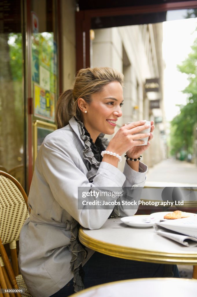 Hispanic woman drinking coffee in outdoor cafe